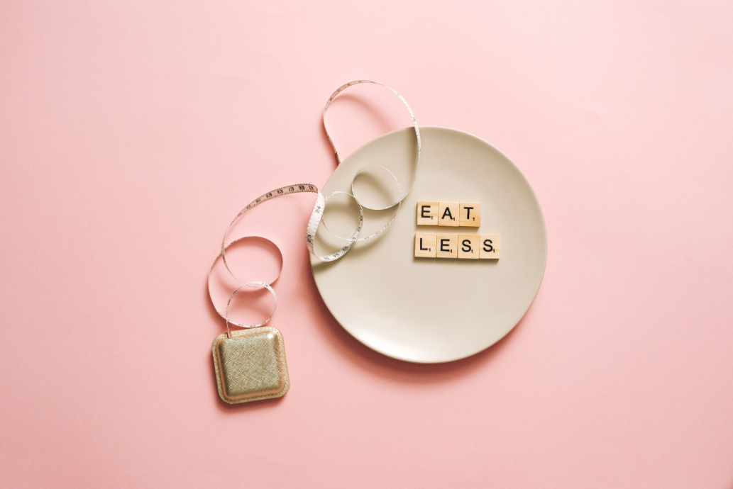 Чинија со порака „Eat Less“ и мерна лента, фотографија поврзана со тоа како да се намали апетитот, контрола на порции и здрави навики во исхраната.